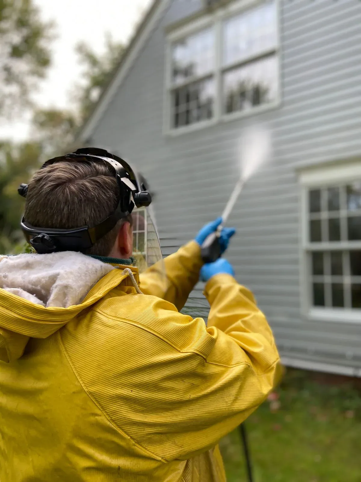 Professional exterior cleaning technician washing home siding with controlled spray
