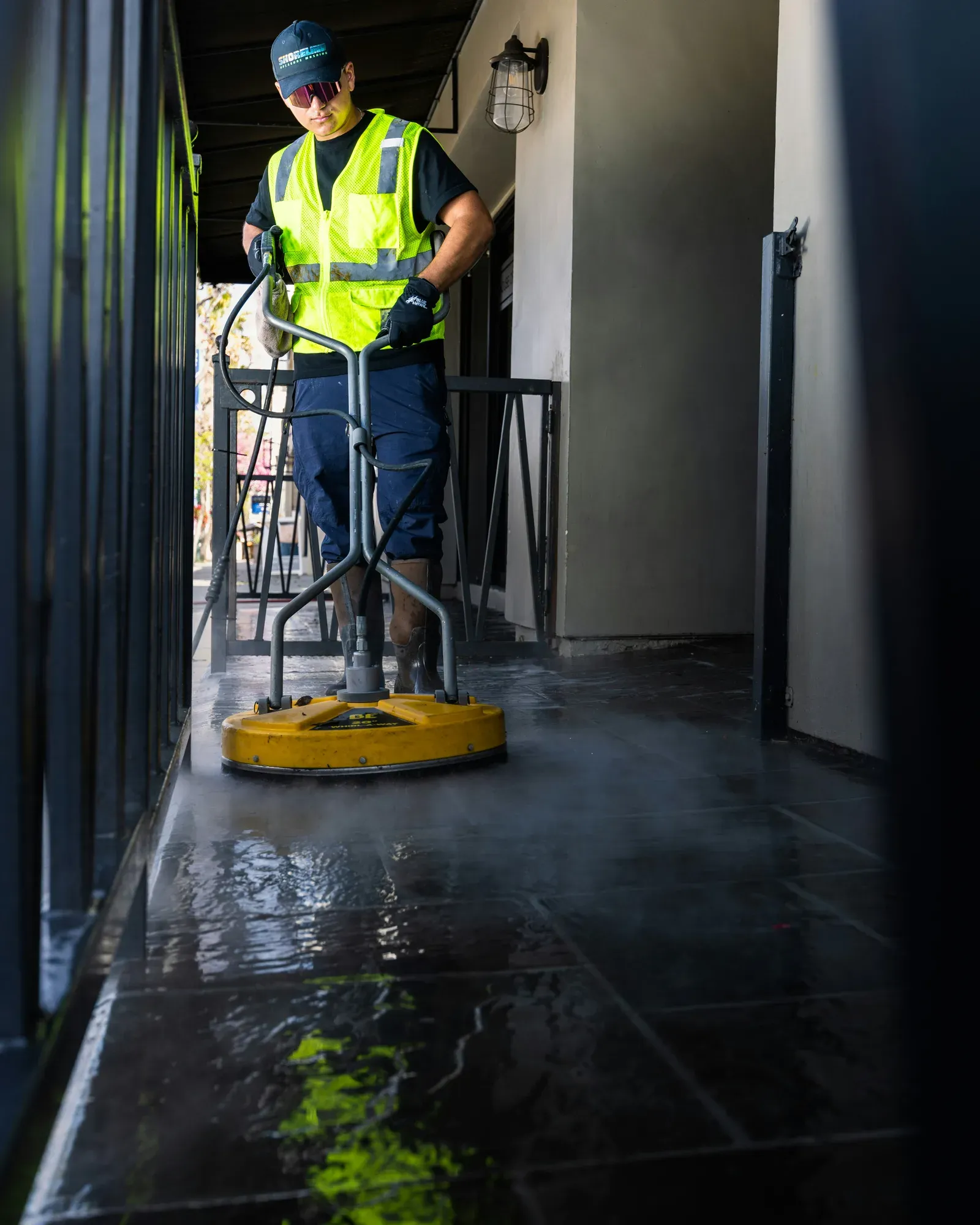 Professional cleaner operating a circular surface cleaner on wet exterior concrete